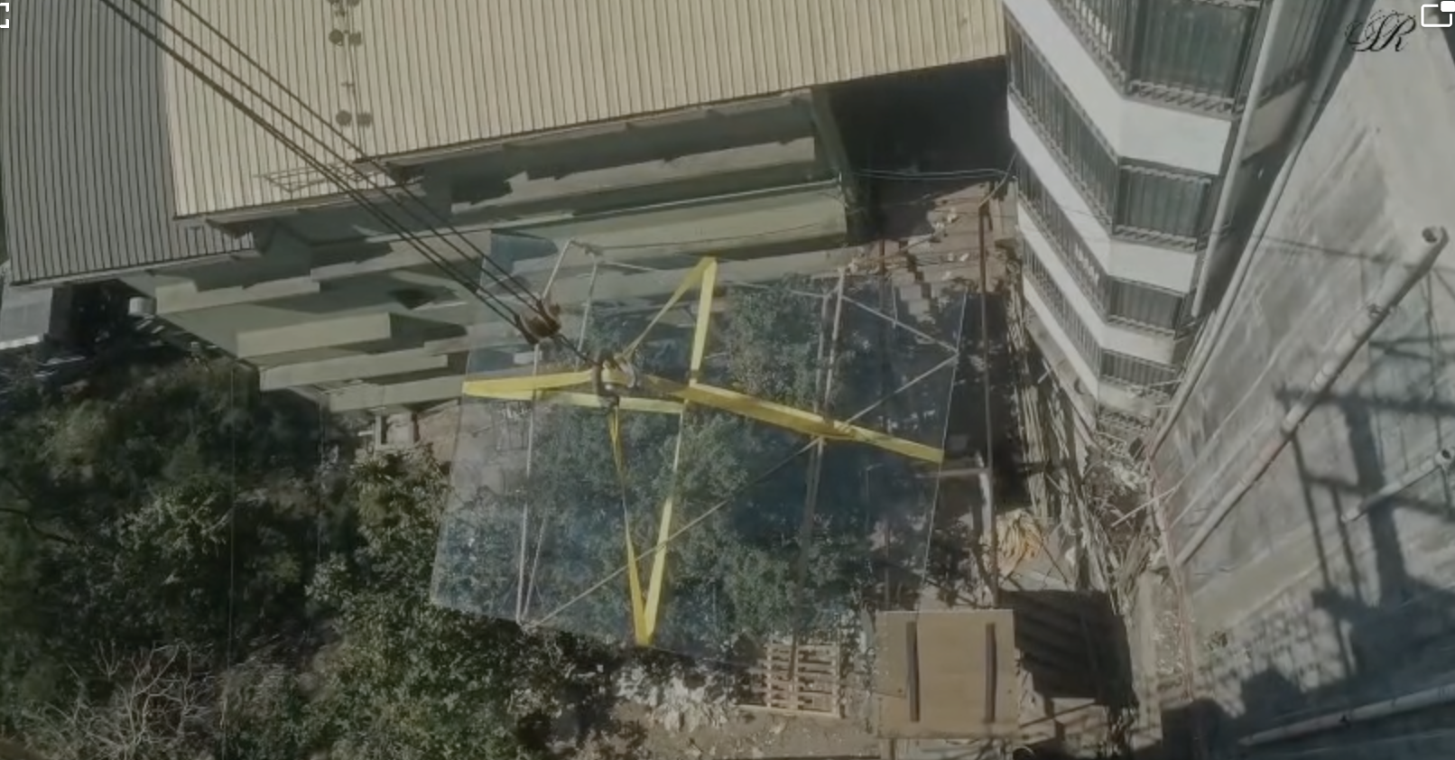 Aerial view of a glass panel being installed between buildings